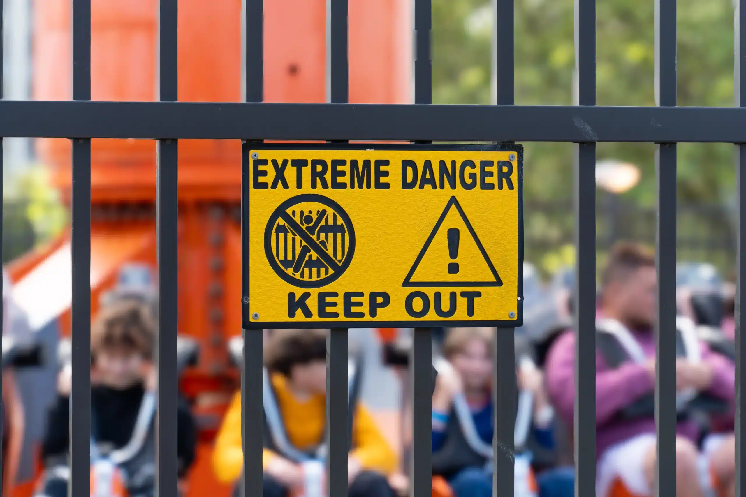 Yellow danger warning sign on a fence at an amusement park ride, showing restricted access and safety hazard conditions