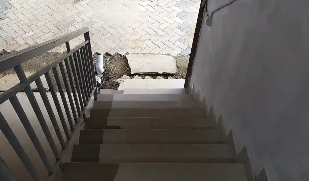 Damaged concrete stairs with a rusty stair railing and broken pavement, showing a broken handrail hazard that can cause falls in New York