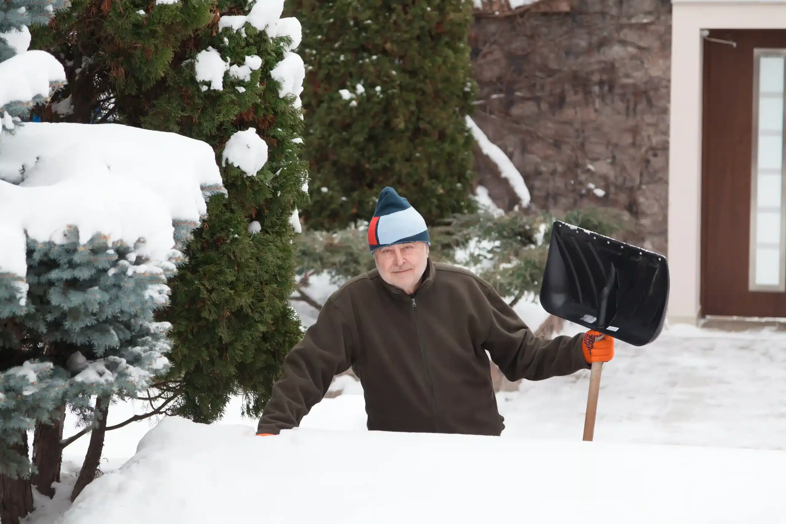 Anciano sosteniendo una pala para nieve en invierno, mostrando cómo quitar la nieve ayuda a prevenir accidentes por resbalones y caídas debido al hielo.